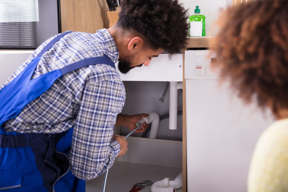 Woman Looking At Male Plumber Cleaning Clogged Pipes 
