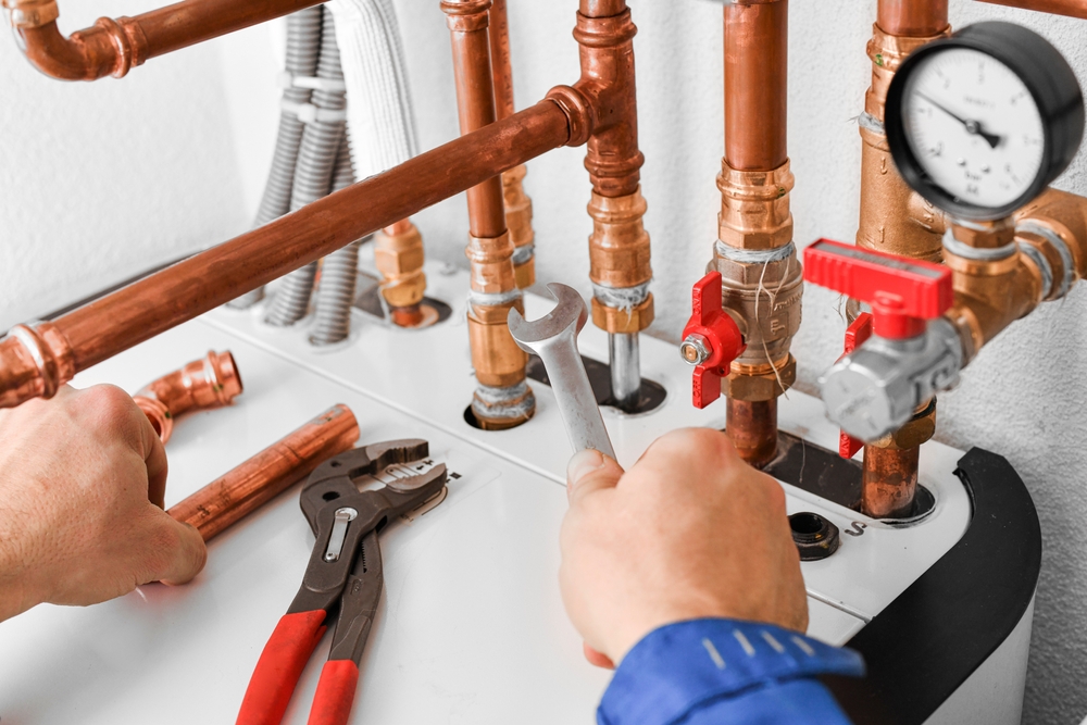 Licensed plumber carefully replacing a section of damaged copper water pipe inside a residential wall utility access panel. Licensed plumber carefully replacing a section of damaged copper water pipe inside a residential wall utility access panel.